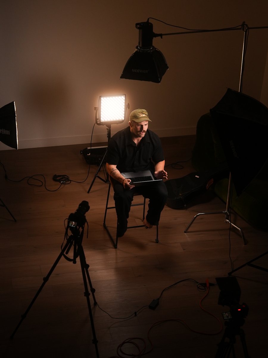 Sam McMacken on set in the Maken studio, laptop open, between a key light and a softbox