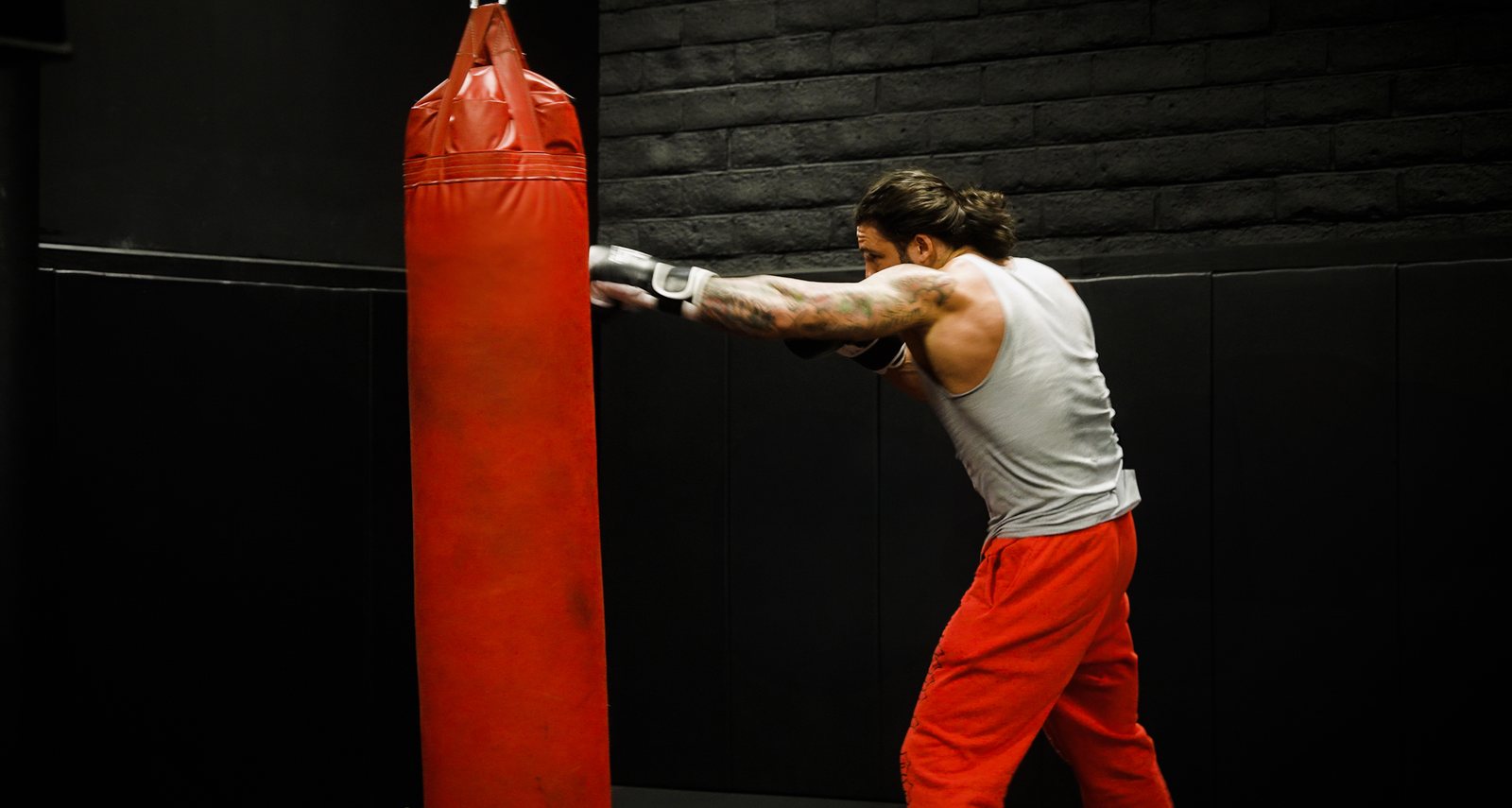 Boxer driving a punch into a red heavy bag in a dark gym, DiagoFit YouTube film