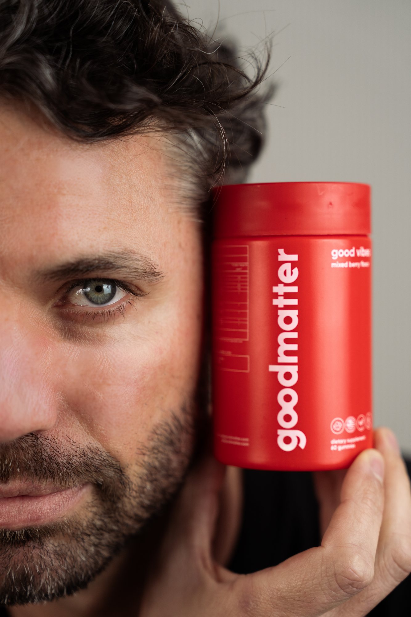 Man holding a red GoodMatter jar beside his face, eye to the lens