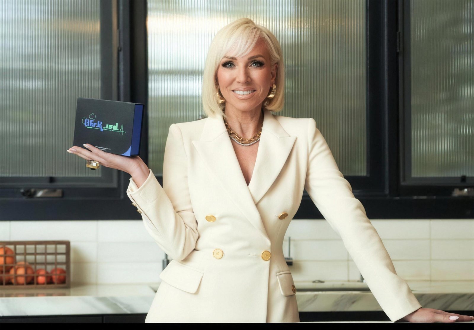 Real Housewives star in a cream suit holding a Liferx box in a kitchen