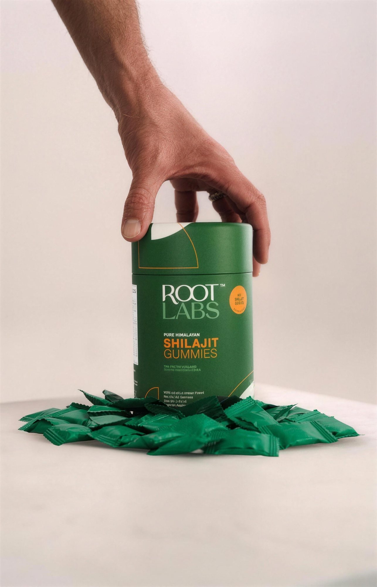 Hand lifting a Root Labs shilajit gummies box from a pile of green gummies