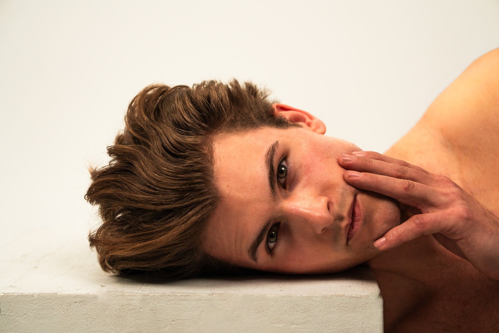 Man resting his head on a plinth with a hand on his cheek, skincare shoot
