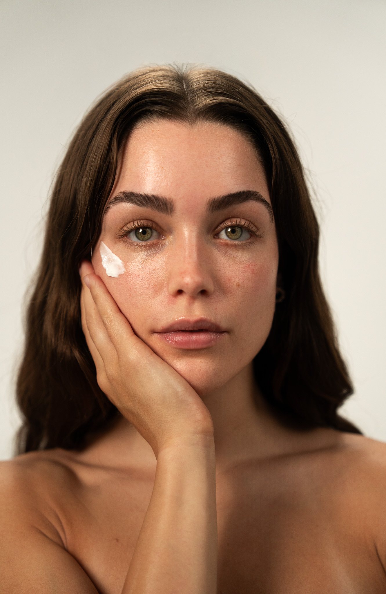 Woman with skincare cream on her cheek, studio portrait